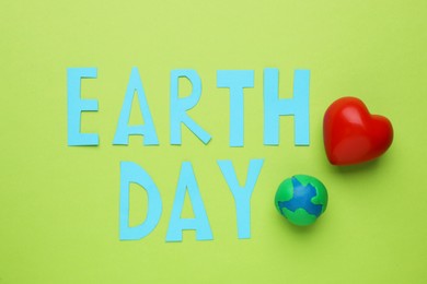 Photo of Phrase Earth Day with model of planet and red heart on green background, flat lay