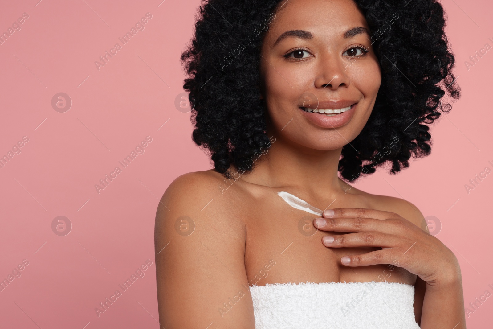 Photo of Young woman applying cream onto body on pink background. Space for text