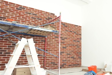 Scaffolding near wall with decorative bricks and tile leveling system in room