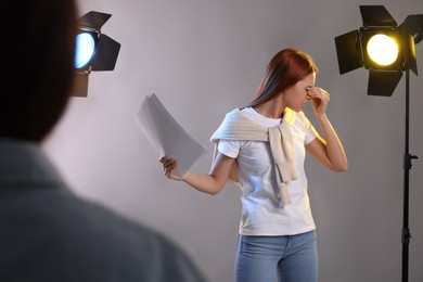 Photo of Emotional woman with script performing in front of casting director against grey background at studio