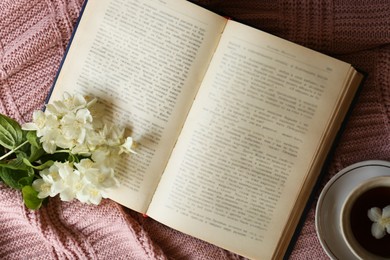 Photo of Beautiful jasmine flowers, open book and cup aromatic tea on pink fabric, flat lay