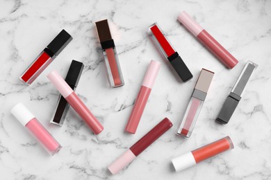 Different lip glosses on white marble table, flat lay
