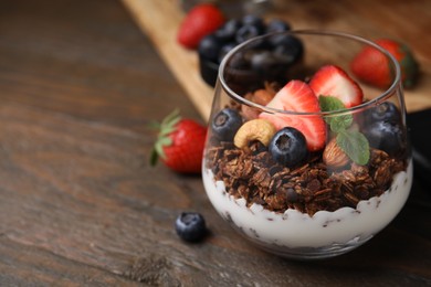 Photo of Tasty granola with berries, nuts and yogurt in glass on wooden table, closeup. Space for text