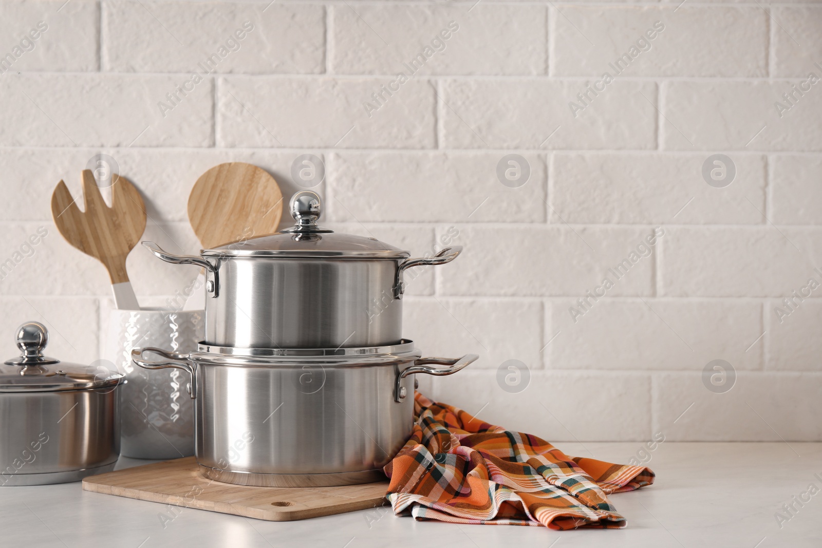 Photo of Set of stainless steel cookware and kitchen utensils on table near white brick wall, space for text