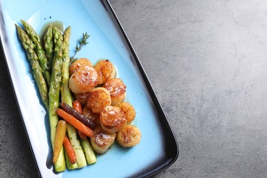 Photo of Delicious fried scallops with asparagus and vegetables on grey table, top view. Space for text