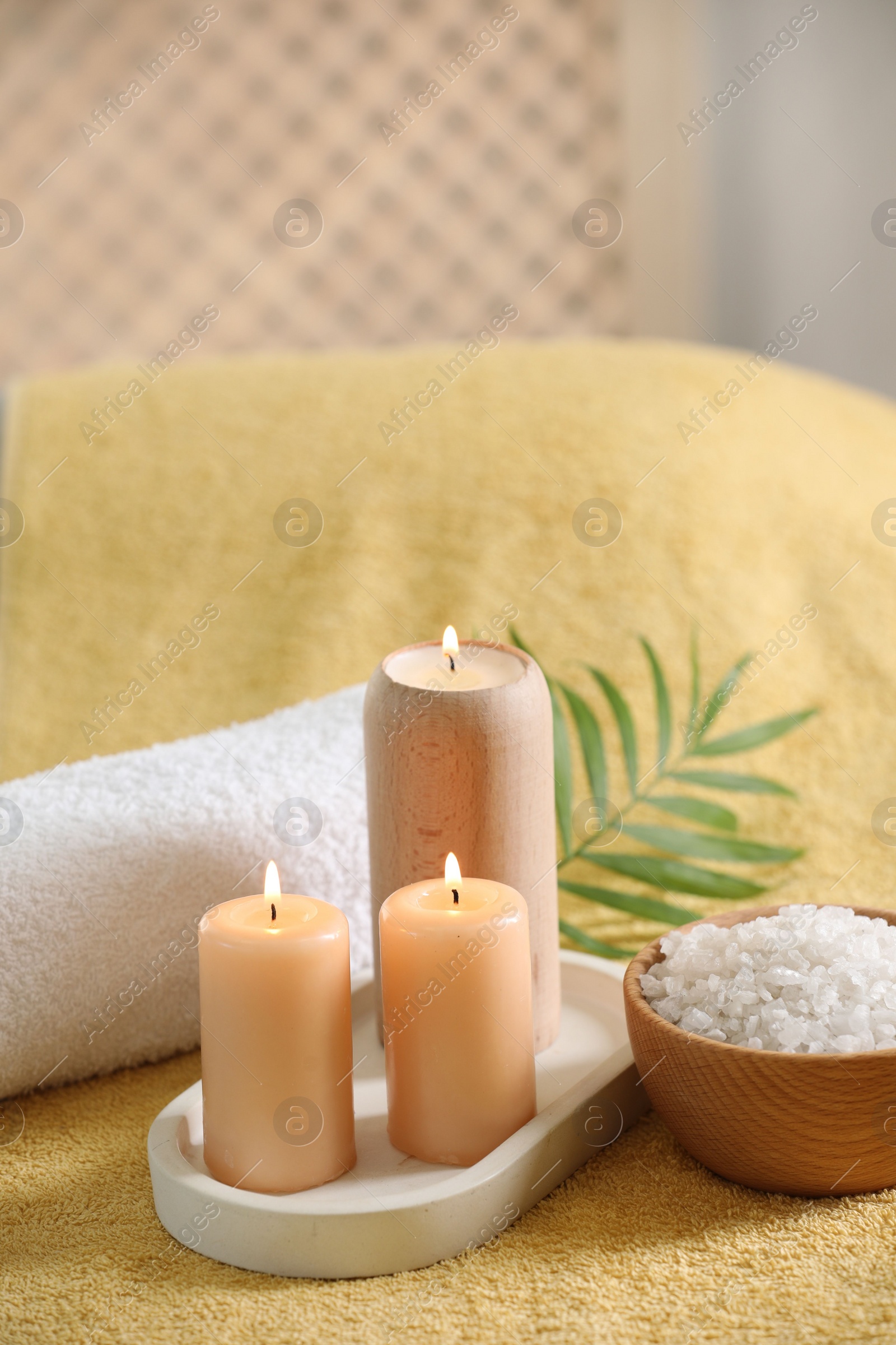 Photo of Spa composition. Burning candles, sea salt and towel on soft yellow surface