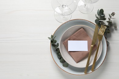 Photo of Stylish setting with cutlery, eucalyptus leaves and blank card on white wooden table, flat lay. Space for text