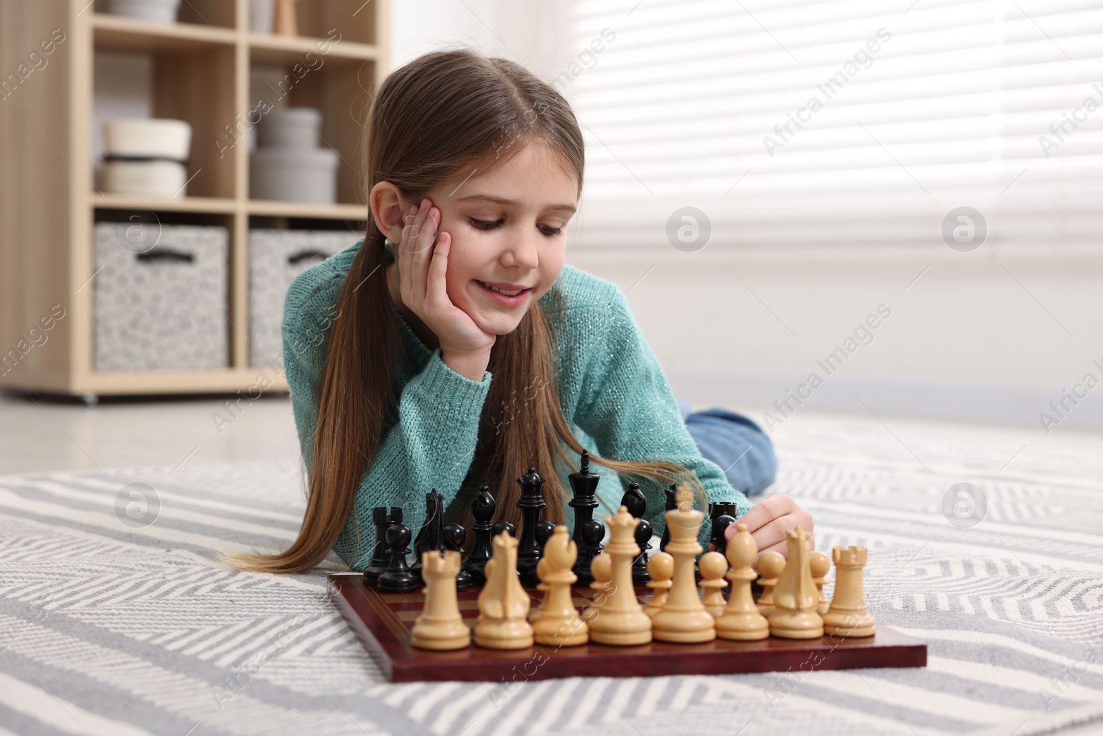 Photo of Cute girl playing chess on floor in room