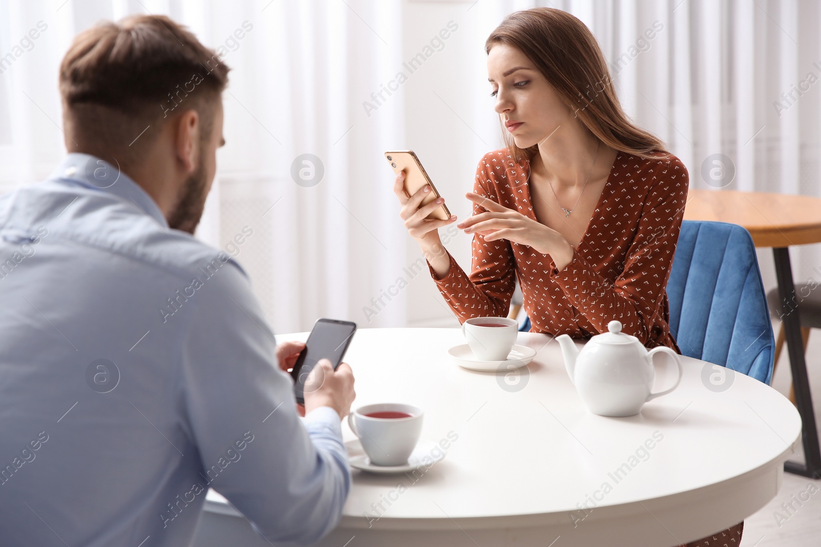 Photo of Couple addicted to smartphones ignoring each other in cafe. Relationship problems