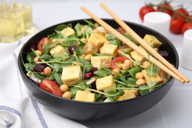 Bowl of tasty salad with tofu, chickpeas and vegetables on white tiled table, closeup