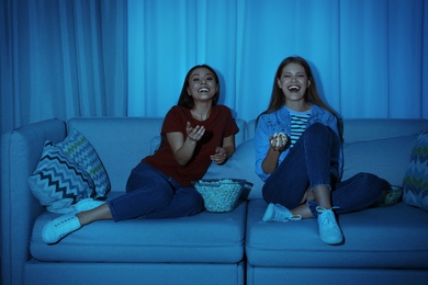 Photo of Friends with bowl of popcorn watching TV together on sofa in dark living room