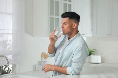 Man drinking tap water from glass in kitchen