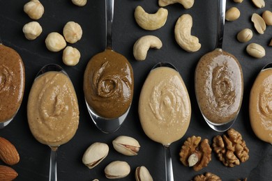 Photo of Tasty nut butters in spoons and raw nuts on dark gray table, flat lay