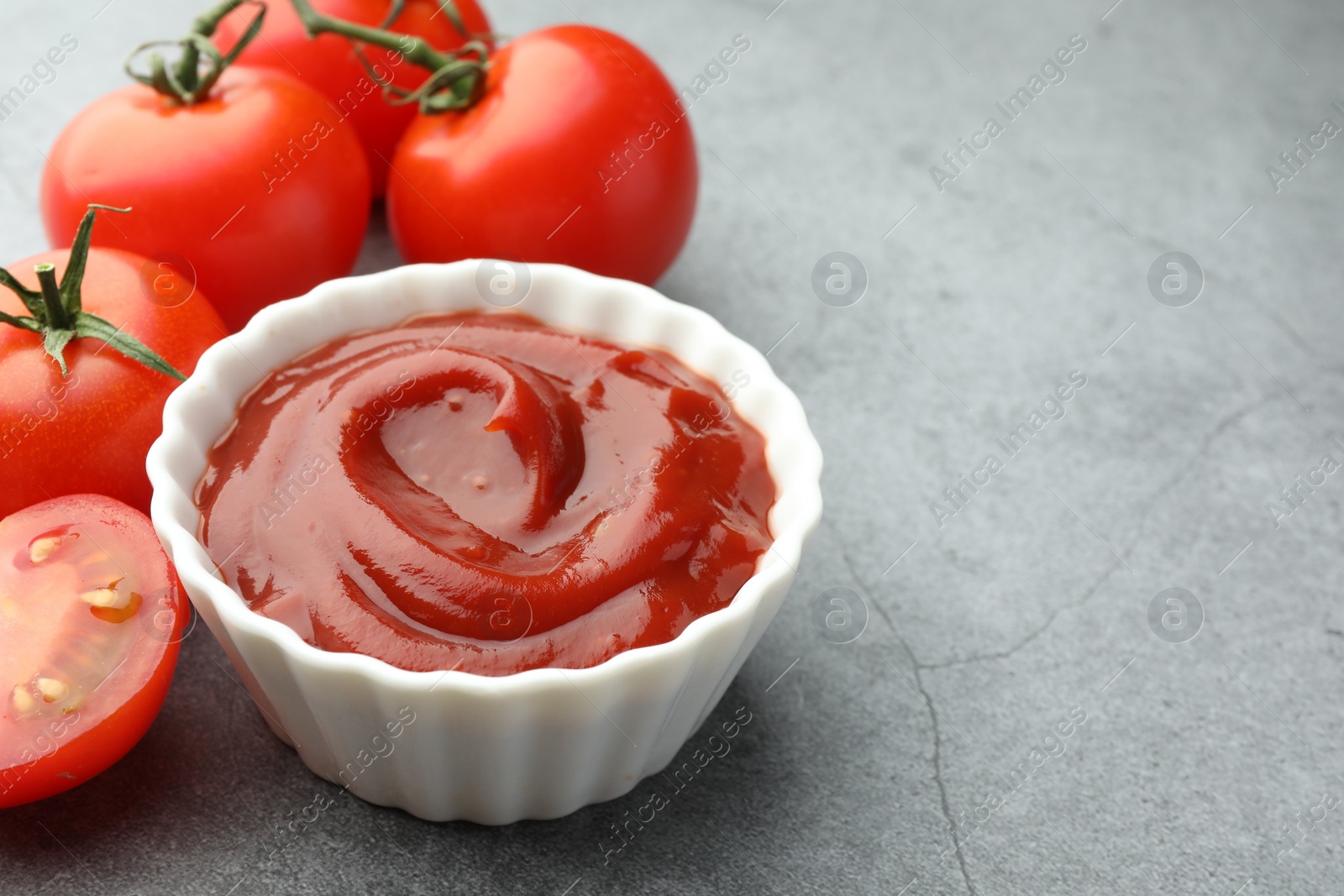 Photo of Bowl of tasty ketchup and tomatoes on light grey table, closeup. Space for text