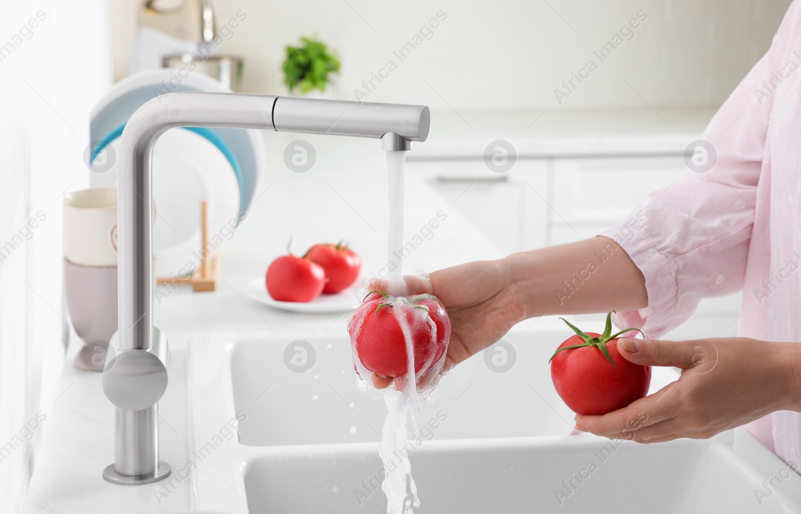 Photo of Woman washing fresh ripe tomatoes under tap water in kitchen, closeup