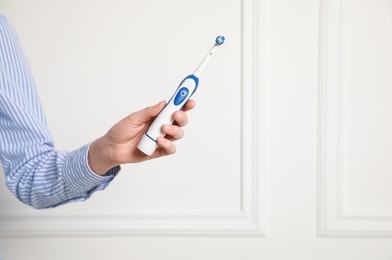 Photo of Woman holding electric toothbrush near white wall, closeup. Space for text
