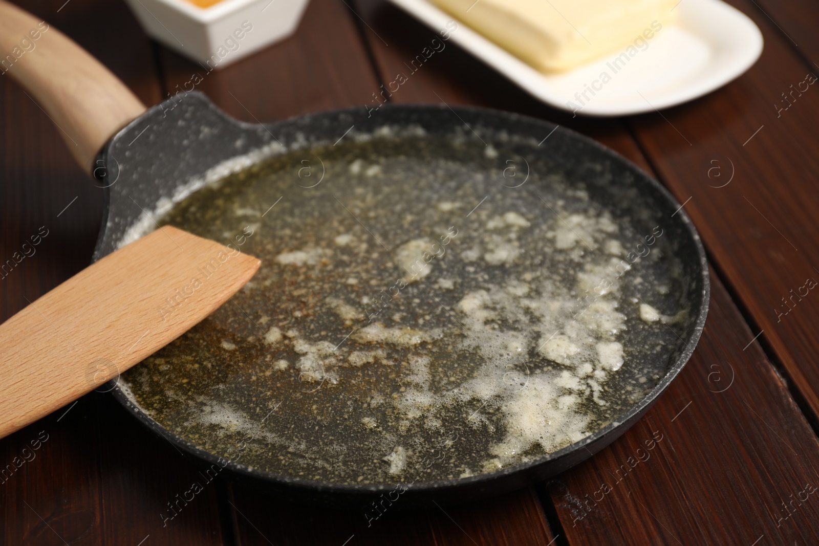 Photo of Melted butter in frying pan and spatula on wooden table, closeup