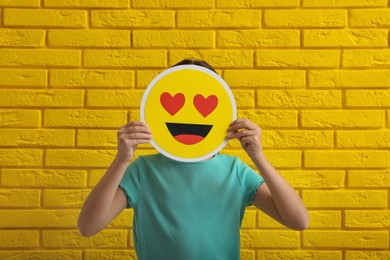 Photo of Little girl covering face with heart eyes emoji near yellow brick wall