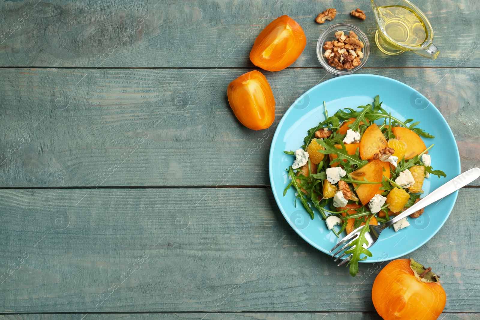 Photo of Delicious persimmon salad served on light blue wooden table, flat lay. Space for text