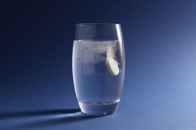 Photo of Effervescent pill dissolving in glass of water on blue background