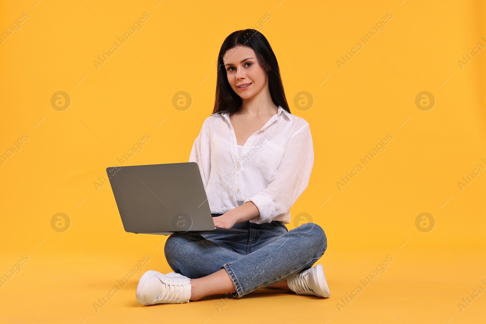 Photo of Smiling student with laptop sitting on yellow background