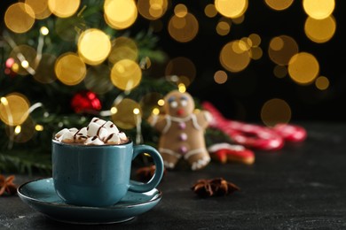 Delicious hot chocolate with marshmallows and syrup on black table against blurred lights, space for text