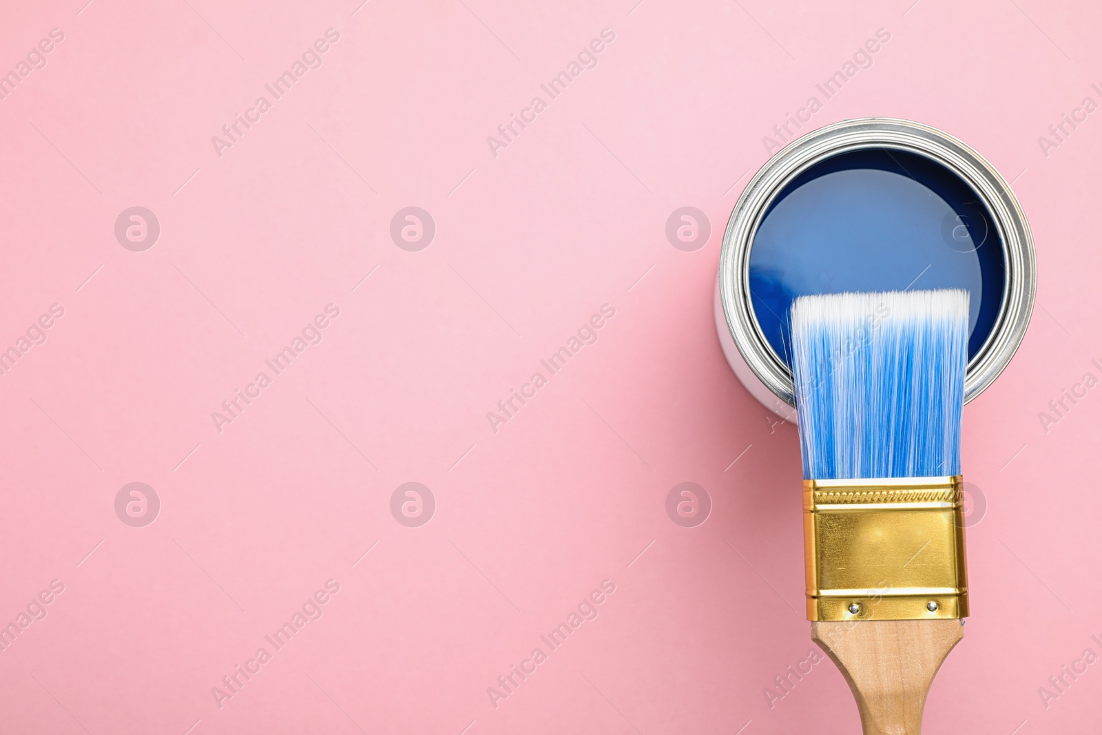 Photo of Open can with blue paint and brush on pink background, top view. Space for text