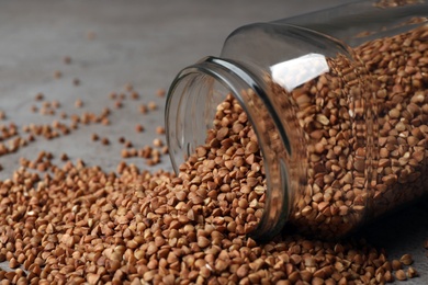 Overturned glass jar with uncooked buckwheat on table, closeup