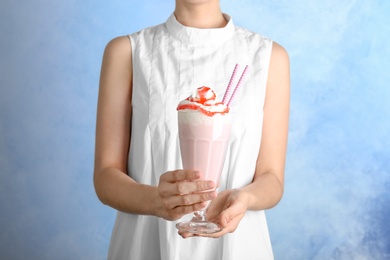 Woman holding glass with delicious milk shake on color background