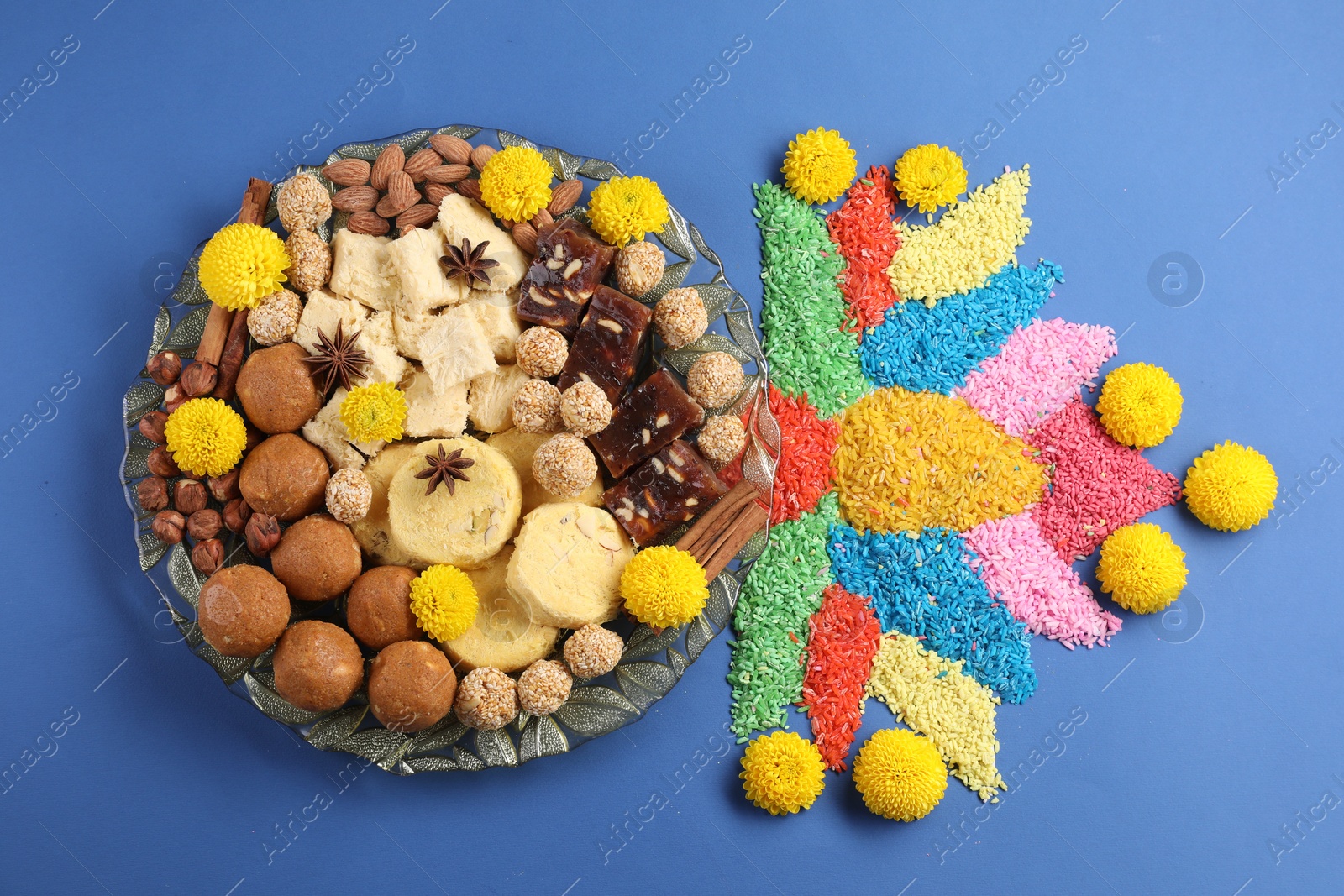 Photo of Diwali celebration. Tasty Indian sweets, colorful rangoli and chrysanthemum flowers on blue table, flat lay