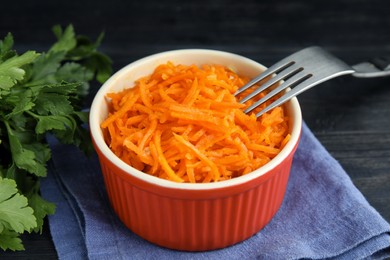 Photo of Delicious Korean carrot salad and parsley on black wooden table