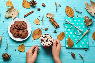 Photo of Woman with cup of hot drink at blue wooden table, top view. Cozy autumn atmosphere