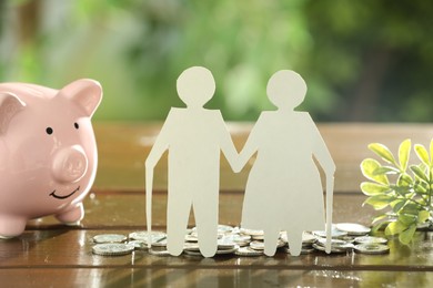 Pension savings. Figure of senior couple, piggy bank, coins and green twigs on wooden table outdoors