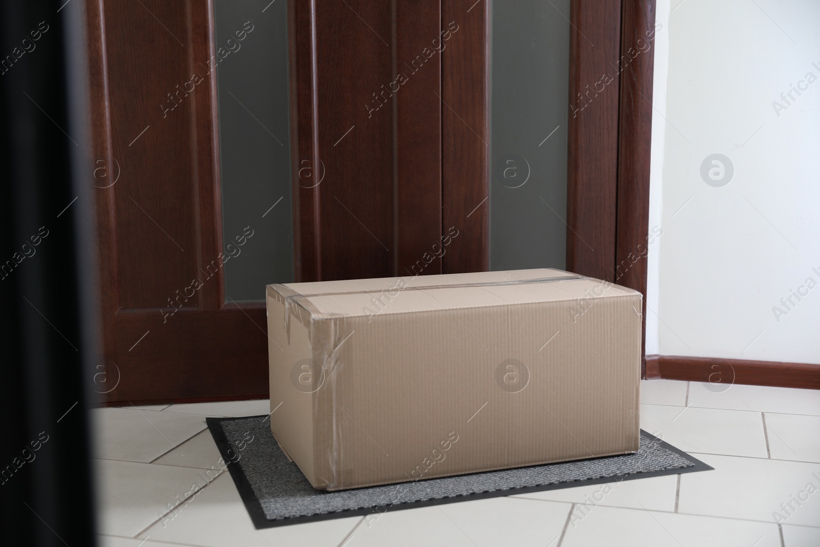 Photo of Cardboard box on rug near door. Parcel delivery service