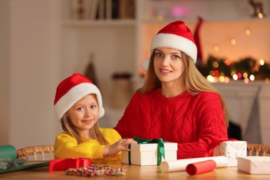 Photo of Christmas presents wrapping. Mother and her little daughter with gift box at table in room