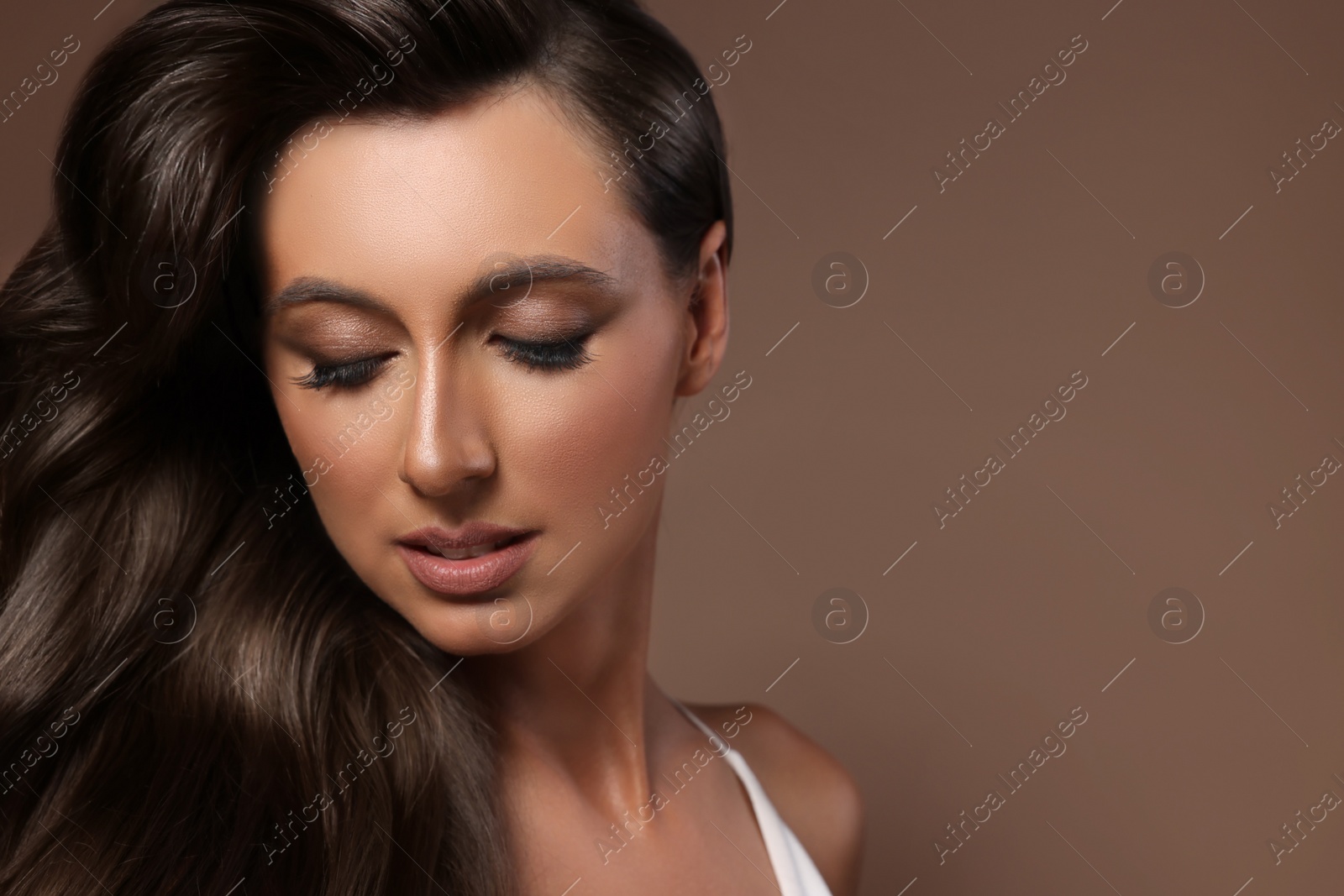 Image of Gorgeous woman with shiny wavy hair on brown background, space for text. Professional hairstyling