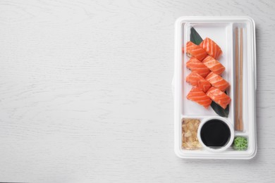 Food delivery. Plastic container with delicious sushi rolls, soy sauce, ginger, wasabi, chopsticks on white wooden table, top view and space for text