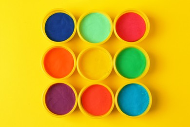 Plastic containers with colorful play dough on yellow background, flat lay