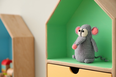Photo of Knitted mouse on house shaped shelf indoors, closeup. Baby room interior design