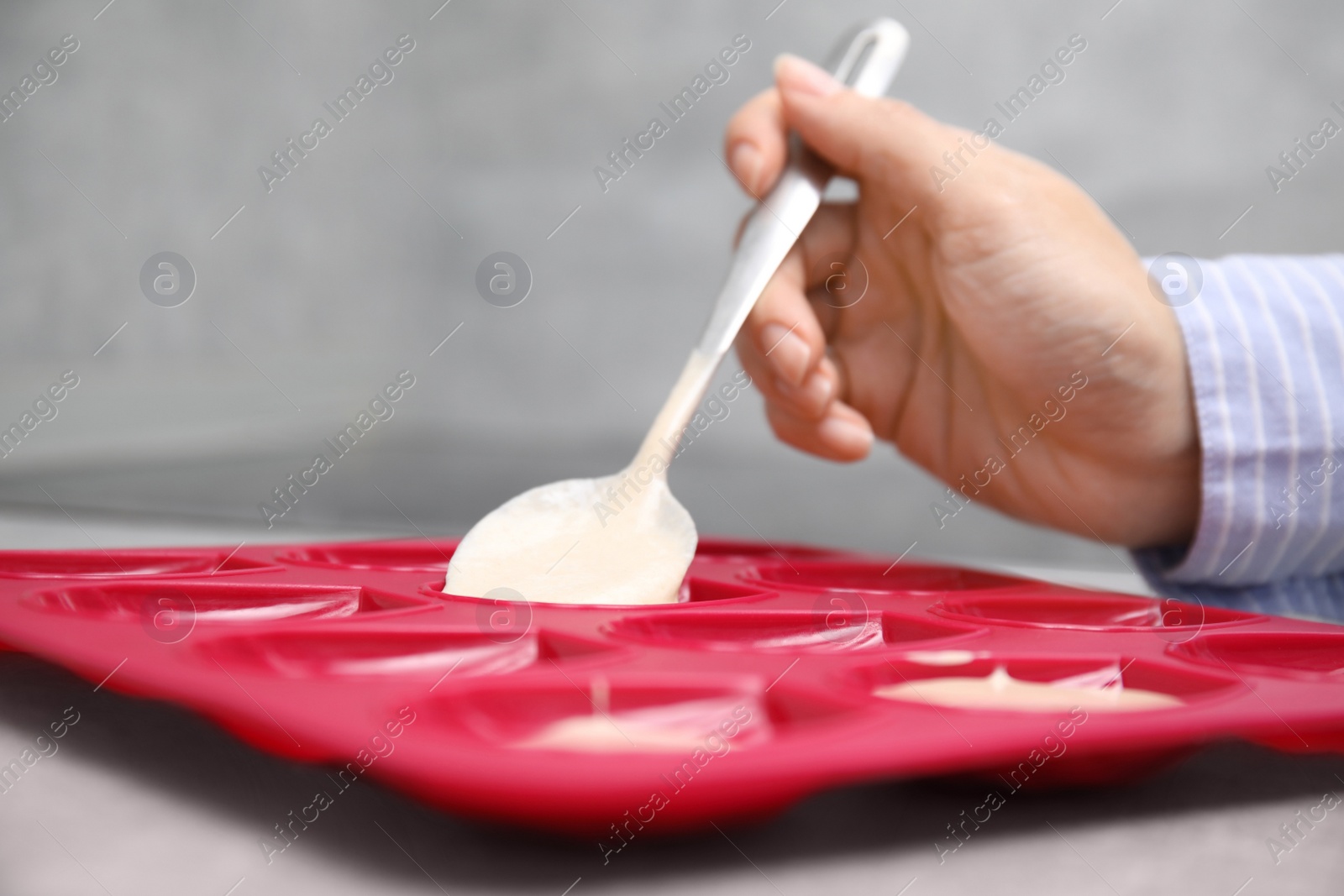 Photo of Woman pouring batter into baking mold at table, closeup. Madeleine cookies