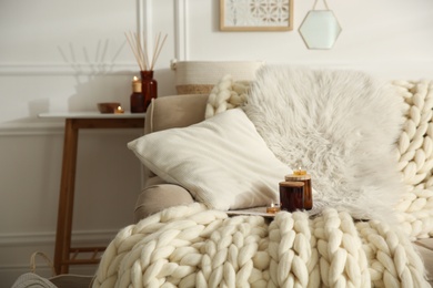 Photo of Candles on beige sofa with knitted blanket. Interior design