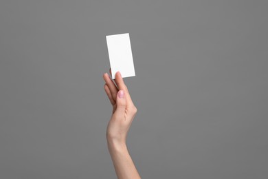 Woman holding blank business card on grey background, closeup. Space for text