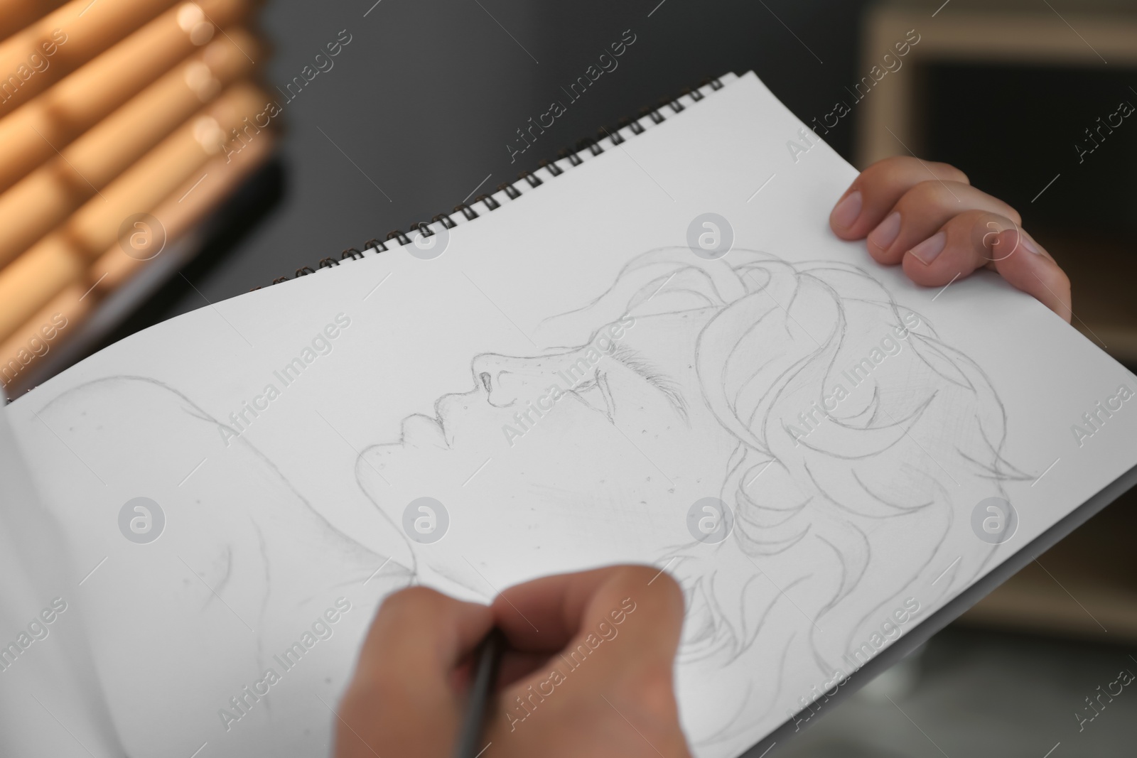 Photo of Man drawing portrait with pencil in notepad indoors, closeup