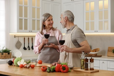 Photo of Happy senior couple with glasses of wine cooking together in kitchen