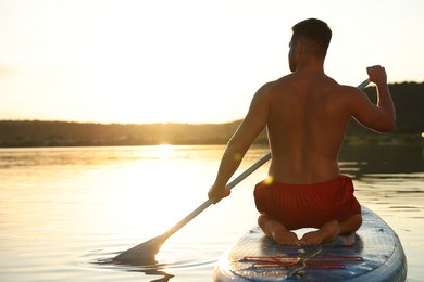 Man paddle boarding on SUP board in river at sunset, back view