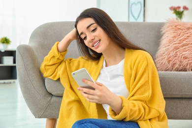 Attractive young woman using mobile phone near sofa at home