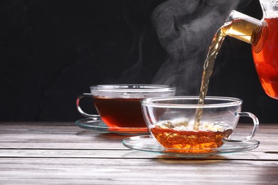 Photo of Pouring tea into glass cup on wooden table against black background, space for text