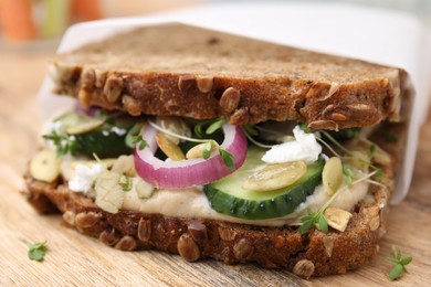 Tasty vegan sandwich with cucumber, onion, hummus and pumpkin seeds on wooden board, closeup