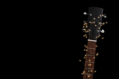 Photo of Guitar with fairy lights on black background, space for text