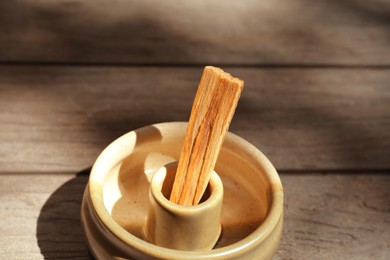 Palo santo stick in holder on wooden table, closeup